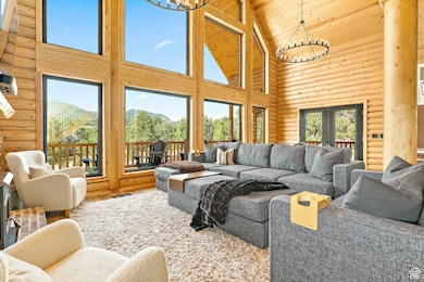 Living room featuring high vaulted ceiling, log walls, a chandelier, wooden ceiling, and french doors