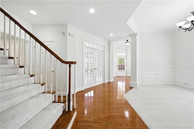 Foyer entrance with stairs, wood finished floors, recessed lighting, a chandelier, and a wainscoted wall
