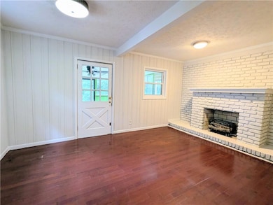 Unfurnished living room featuring beam ceiling, crown molding, dark wood finished floors, a fireplace, and a textured ceiling