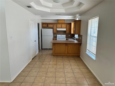 Kitchen featuring a peninsula, brown cabinetry, white appliances, and light tile patterned flooring