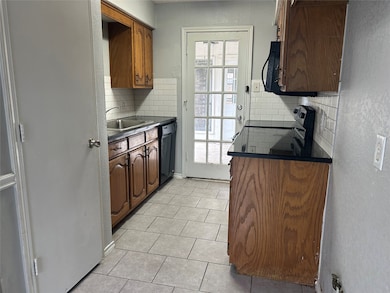 Kitchen with a textured wall, tasteful backsplash, dark countertops, light tile patterned floors, and black dishwasher