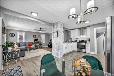 Kitchen with wall chimney range hood, ceiling fan with notable chandelier, appliances with stainless steel finishes, light hardwood / wood-style floors, and white cabinetry