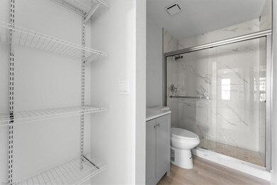 Bathroom with toilet, a marble finish shower, wood finished floors, and vanity