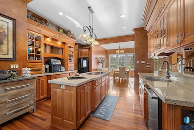 This spacious kitchen showcases rich wood cabinetry, granite countertops, and dual islands—one with a built-in cooktop. Pendant lighting and crown molding add elegance, while expansive windows flood the space with natural light, complementin