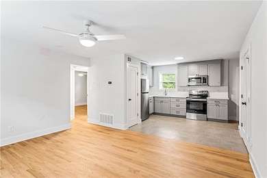 Kitchen featuring appliances with stainless steel finishes, gray cabinets, ceiling fan, tasteful backsplash, and light countertops