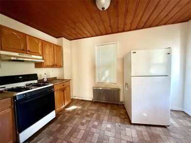 Kitchen featuring gas range oven, brick patterned floors, freestanding refrigerator, radiator heating unit, and under cabinet range hood