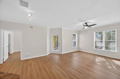 A bright and spacious living area featuring fresh neutral tones, crown molding, and wood-look flooring that adds warmth and style. Large windows fill the space with natural light, creating an airy, inviting atmosphere.