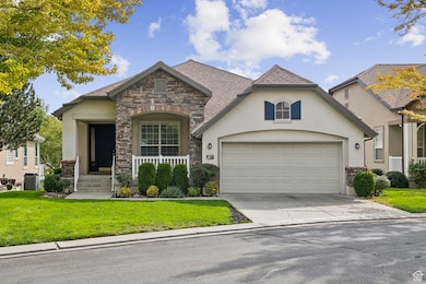 View of front facade featuring stucco siding, concrete driveway, a front yard, and stone siding