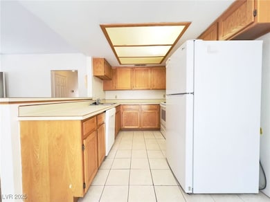 Kitchen featuring white appliances, light countertops, brown cabinets, light tile patterned floors, and a peninsula