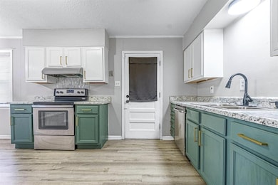 Kitchen with green cabinetry, white cabinetry, stainless steel appliances, light wood finished floors, and a textured ceiling