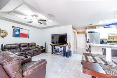 Living room featuring a textured ceiling, a tray ceiling, light tile floors, and ceiling fan