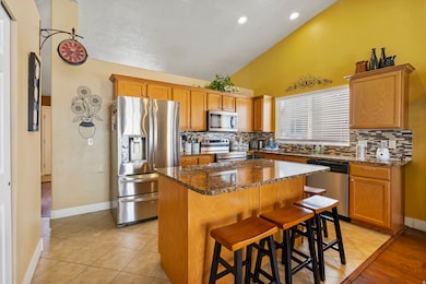 Kitchen featuring stainless steel appliances, a kitchen bar, dark stone counters, a kitchen island, and decorative backsplash