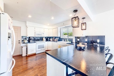 Kitchen with white appliances, a peninsula, dark countertops, tasteful backsplash, and recessed lighting
