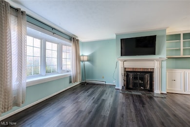 Unfurnished living room with dark wood-type flooring, a brick fireplace, crown molding, and a baseboard heating unit