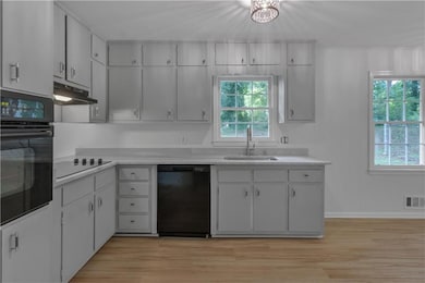 Kitchen featuring black appliances, a sink, under cabinet range hood, light countertops, and light wood-style flooring