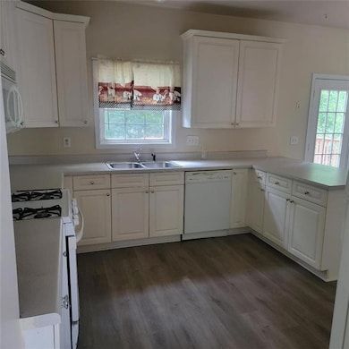 Kitchen with white appliances, dark wood finished floors, a peninsula, white cabinetry, and light countertops