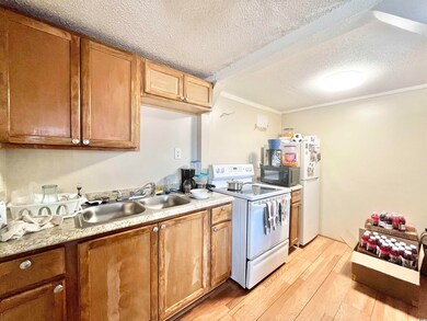 Kitchen featuring white electric stove, light wood-style floors, a textured ceiling, a sink, and ornamental molding