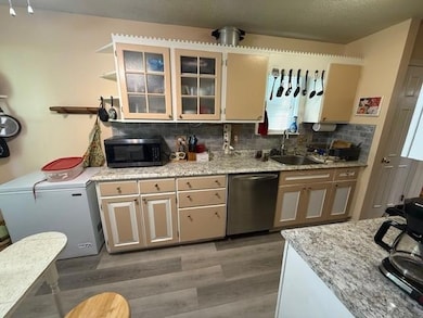 Kitchen with stainless steel appliances, light wood-style floors, decorative backsplash, glass insert cabinets, and light stone counters