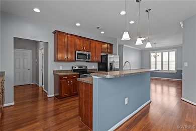 Kitchen featuring stainless steel appliances, dark wood-style flooring, a chandelier, a center island with sink, and pendant lighting