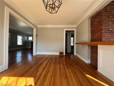 Unfurnished living room with ornamental molding, an inviting chandelier, dark wood-type flooring, and brick wall