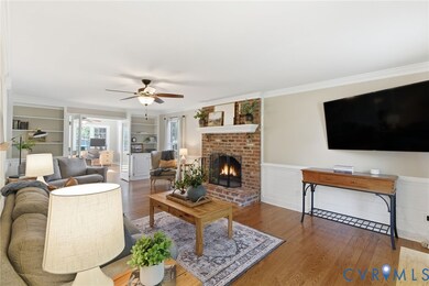 Living area with wood finished floors, a fireplace, crown molding, built in features, and ceiling fan