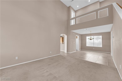 Unfurnished living room with light colored carpet, arched walkways, light tile patterned floors, a towering ceiling, and a chandelier