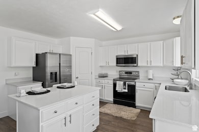 Kitchen with white cabinetry, stainless steel appliances, dark wood-style flooring, a kitchen island, and light stone counters