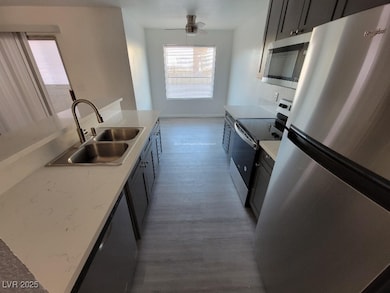 Kitchen with stainless steel appliances, a sink, light wood finished floors, a ceiling fan, and baseboards