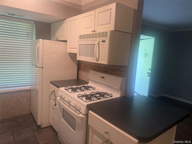 Kitchen featuring dark countertops, white appliances, white cabinetry, and crown molding
