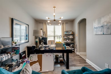 Home office featuring a chandelier, arched walkways, wood finished floors, and a textured wall