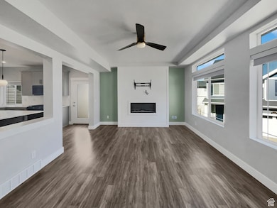 Unfurnished living room with dark wood finished floors, a glass covered fireplace, and a healthy amount of sunlight