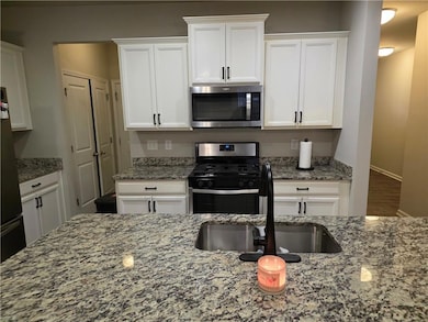 Kitchen with stainless steel appliances, white cabinets, and light stone counters