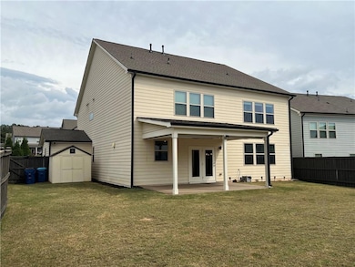 Back of house featuring a storage unit, a fenced backyard, a patio, and roof with shingles