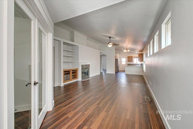 Unfurnished living room with a textured ceiling, a ceiling fan, dark wood-style floors, a premium fireplace, and vaulted ceiling