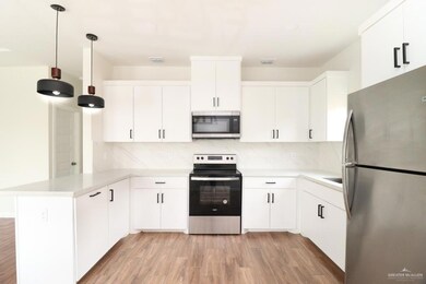 Kitchen featuring decorative backsplash, appliances with stainless steel finishes, decorative light fixtures, light hardwood / wood-style flooring, and white cabinetry