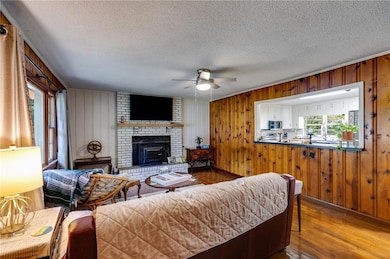 Living room with plenty of natural light, ceiling fan, wood walls, wood finished floors, and a textured ceiling