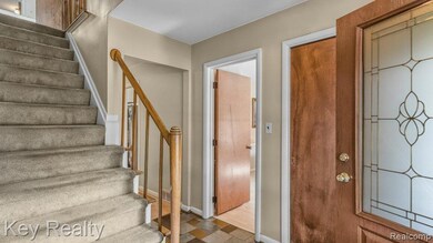 Welcoming entryway with carpeted staircase, wood handrail, and decorative glass door—sets a warm tone with neutral finishes and natural flow into the main level