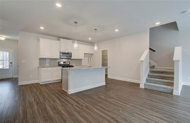 Kitchen with decorative backsplash, stainless steel appliances, pendant lighting, white cabinets, and a center island with sink