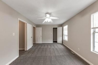 Unfurnished bedroom with multiple windows, dark colored carpet, and ceiling fan
