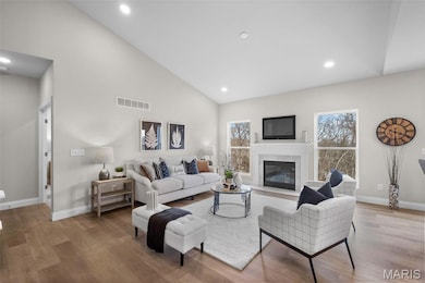 Living area featuring wood finished floors, a glass covered fireplace, recessed lighting, and high vaulted ceiling