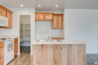 Kitchen featuring white appliances, a center island with sink, light wood-type flooring, recessed lighting, and light brown cabinetry