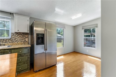 Kitchen with stainless steel fridge, a textured ceiling, light wood-type flooring, backsplash, and white cabinets
