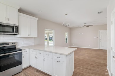 Kitchen featuring stainless steel appliances, a peninsula, decorative backsplash, light countertops, and a ceiling fan