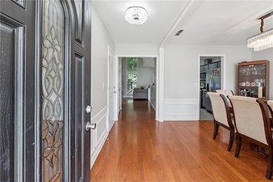 Foyer entrance featuring a chandelier, wood finished floors, wainscoting, and a decorative wall