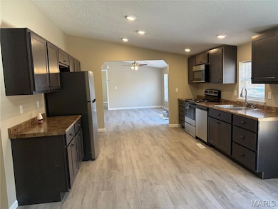 Kitchen with arched walkways, dark countertops, stainless steel appliances, ceiling fan, and light wood-style floors
