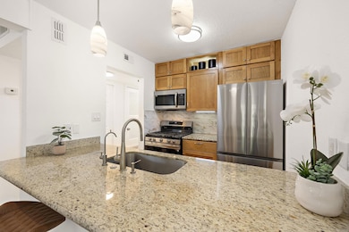 Kitchen featuring appliances with stainless steel finishes, backsplash, light stone counters, hanging light fixtures, and a breakfast bar area