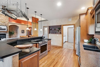Kitchen with appliances with stainless steel finishes, dark countertops, hardwood flooring, custom wood cabinetry