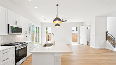 Kitchen with appliances with stainless steel finishes, white cabinetry, decorative light fixtures, a center island with sink, and recessed lighting