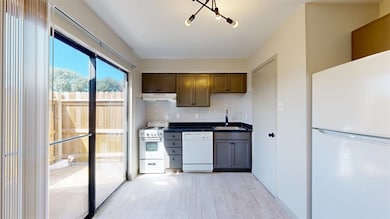 Kitchen with white appliances, dark countertops, a sink, under cabinet range hood, and backsplash