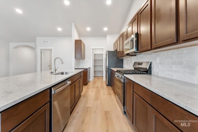 Kitchen featuring appliances with stainless steel finishes, decorative backsplash, light wood-type flooring, light stone countertops, and recessed lighting